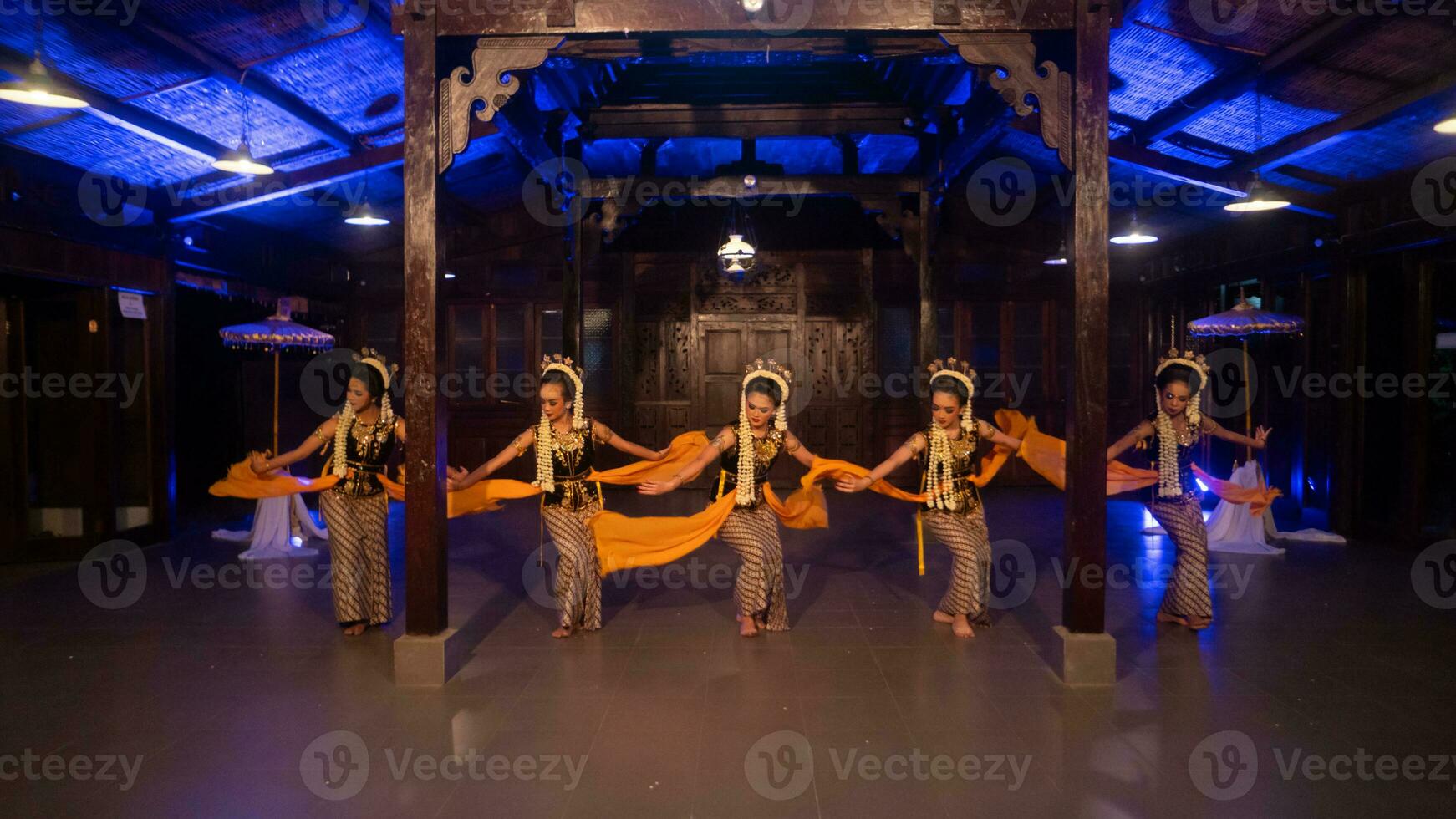 en grupp av Sundanesiska dansare i gul kostymer dansa en traditionell dansa i främre av en blå ljus foto