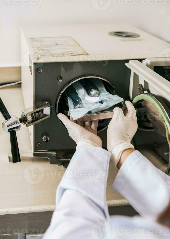 stänga upp av händer med dental autoklav sterilisator maskin. tandläkare händer sterilisering verktyg med autoklav, tandläkare med dental autoklav, stänga upp av tandläkare med ånga sterilisator foto