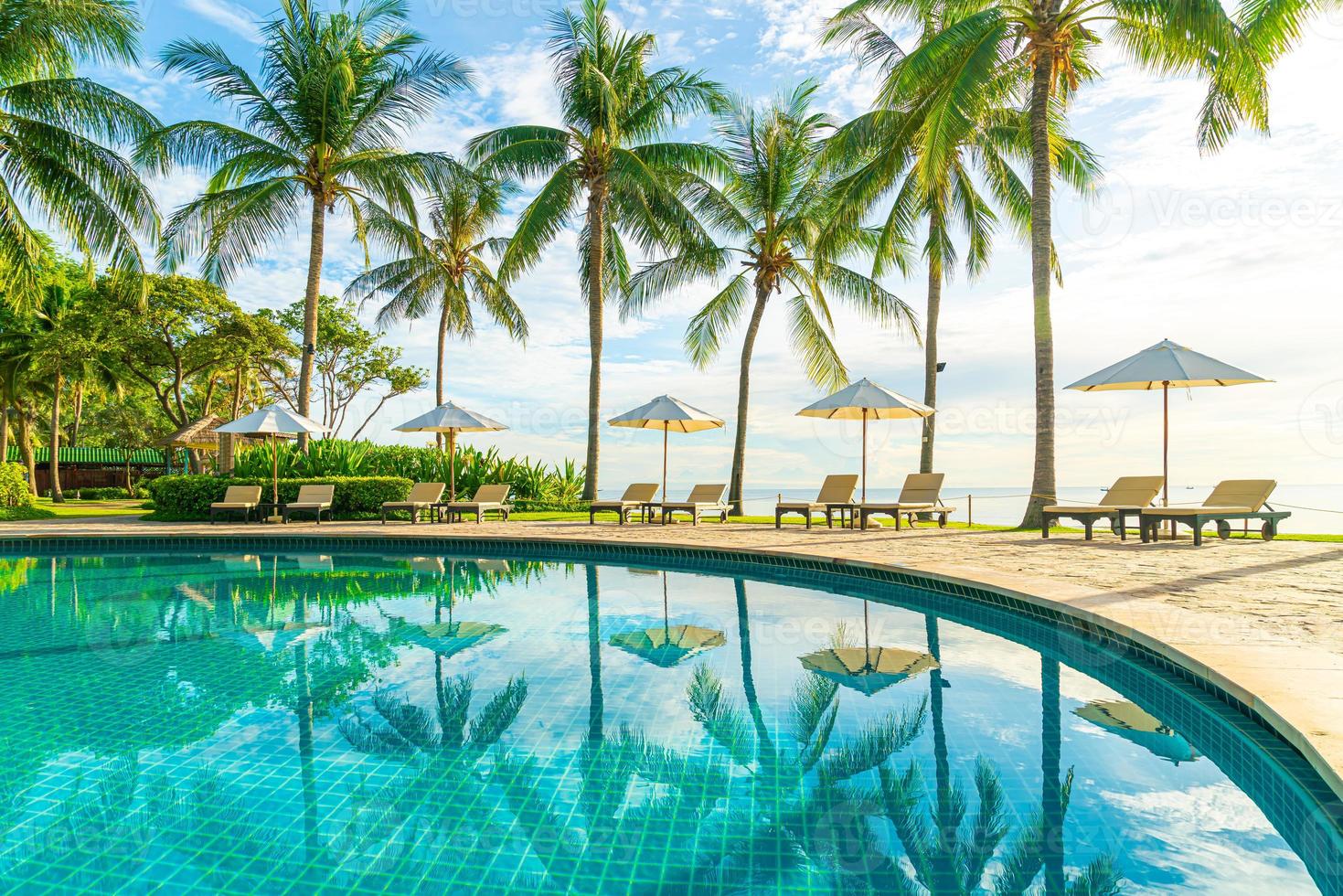 vackert lyxigt paraply och stol runt utomhuspoolen på hotellet och resort med kokospalmer på solnedgången eller soluppgångshimlen foto