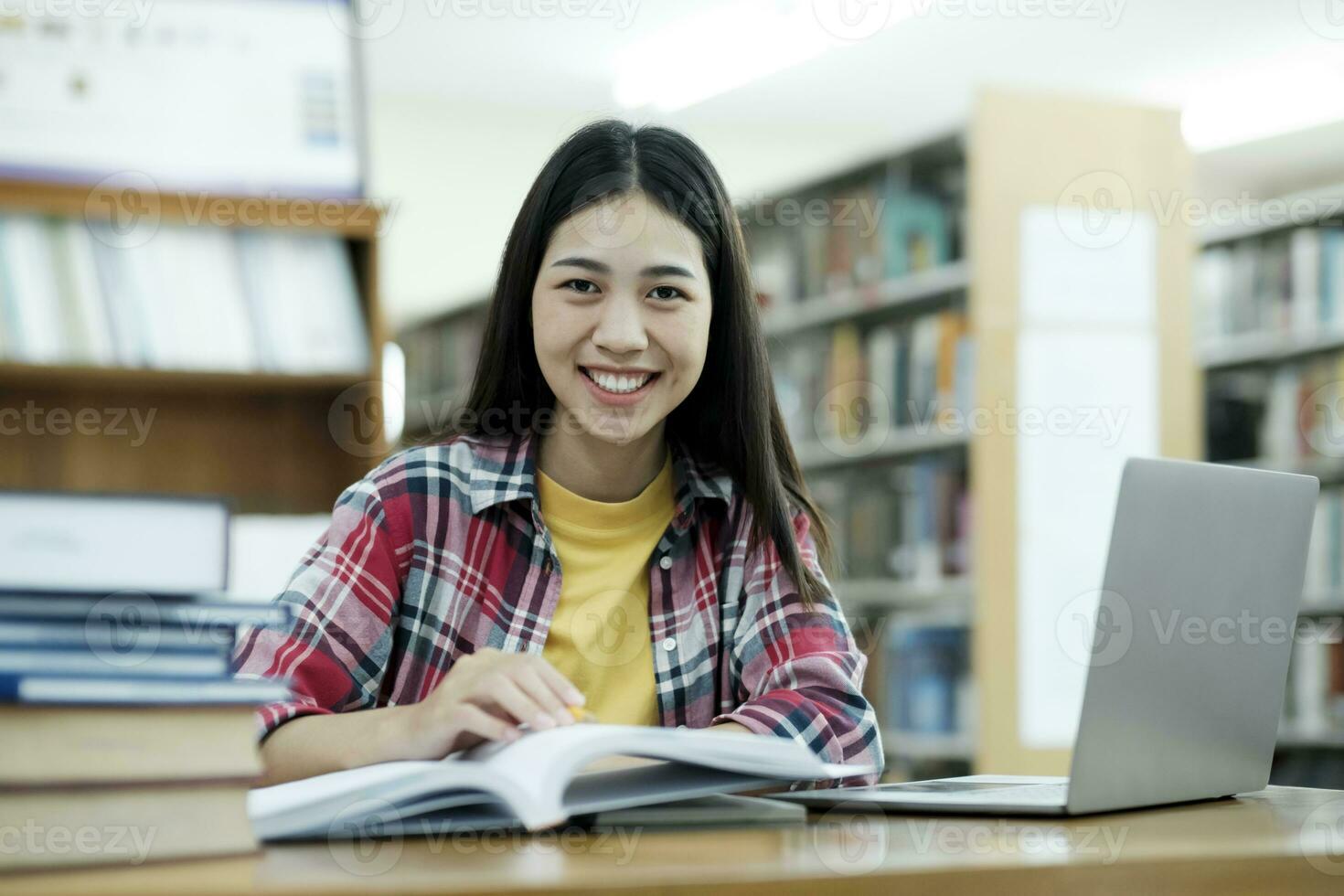 porträtt av en smart skön asiatisk flicka studing och läsning text böcker leende ser på kamera. foto