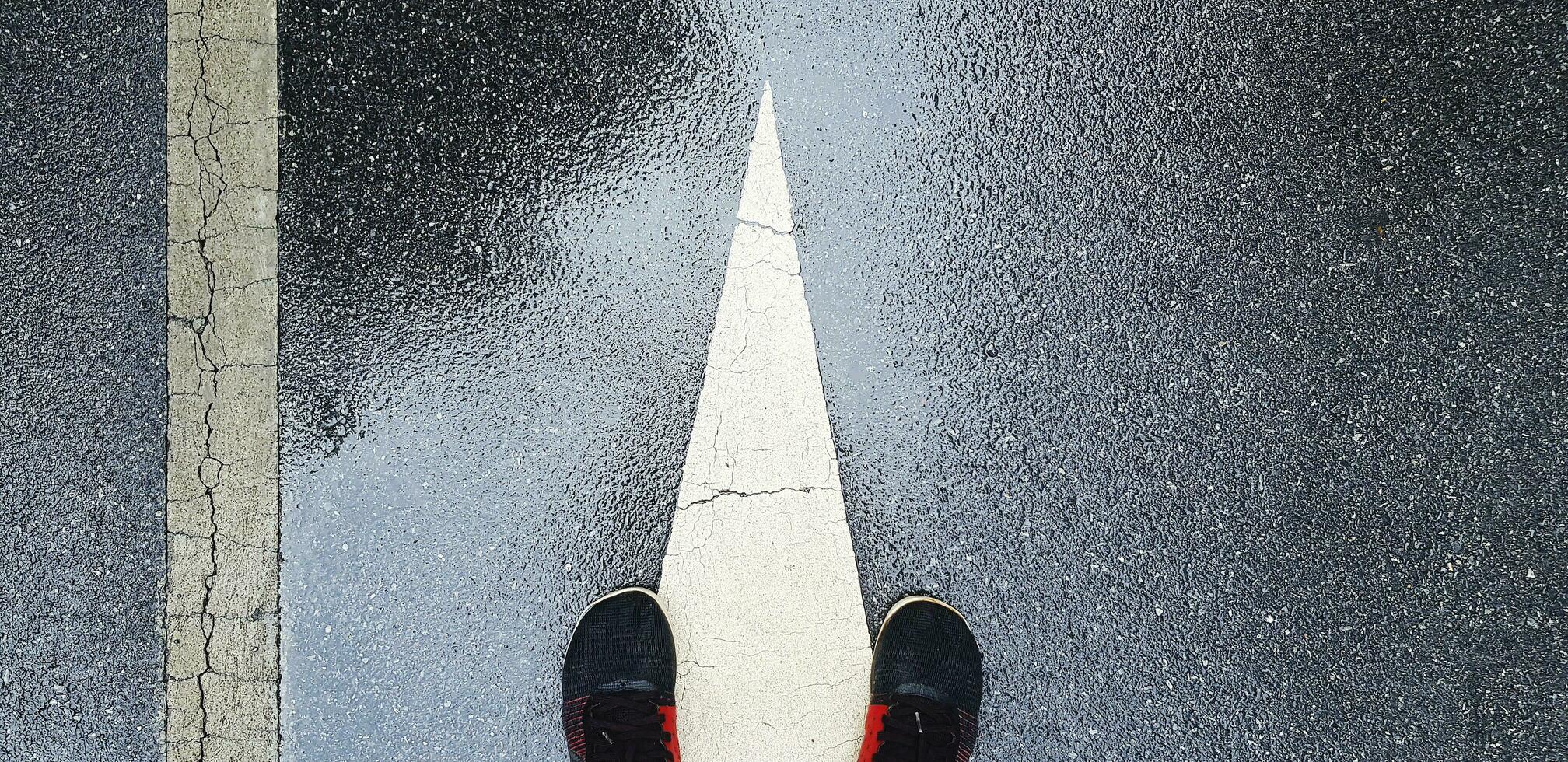 topp se eller platt lägga av gymnastiksko eller löpning skor på våt gata eller väg med vit slutet av riktning tecken och linje med kopia Plats. skojar och övning efter regnar. foto