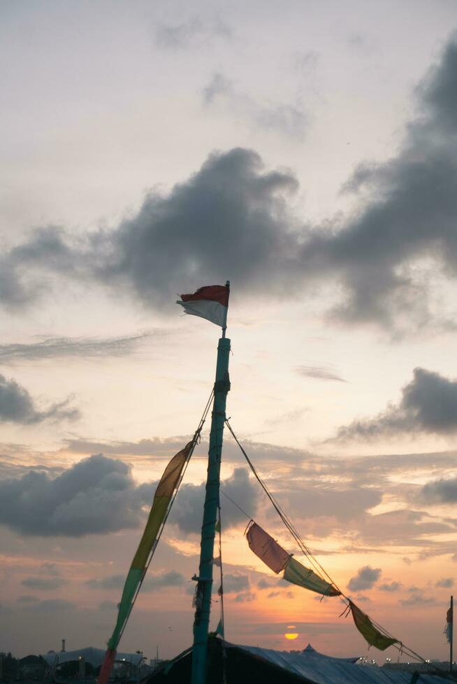 de båt mast, på topp av som de indonesiska flagga är vinka, som skymning ankommer med skön kväll moln. foto