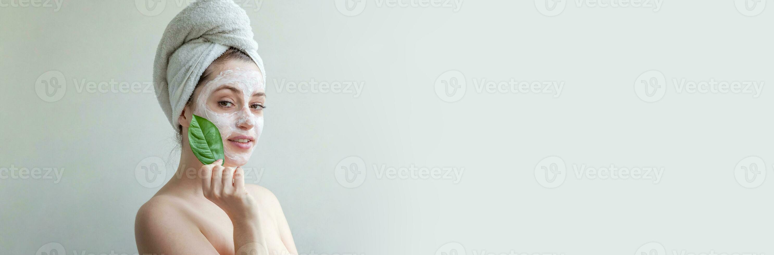 skönhet porträtt av kvinna i handduk på huvud med vit närande mask eller creme på ansikte och grön blad i hand, vit bakgrund isolerat. hudvård rensning eco organisk kosmetisk spa begrepp. foto