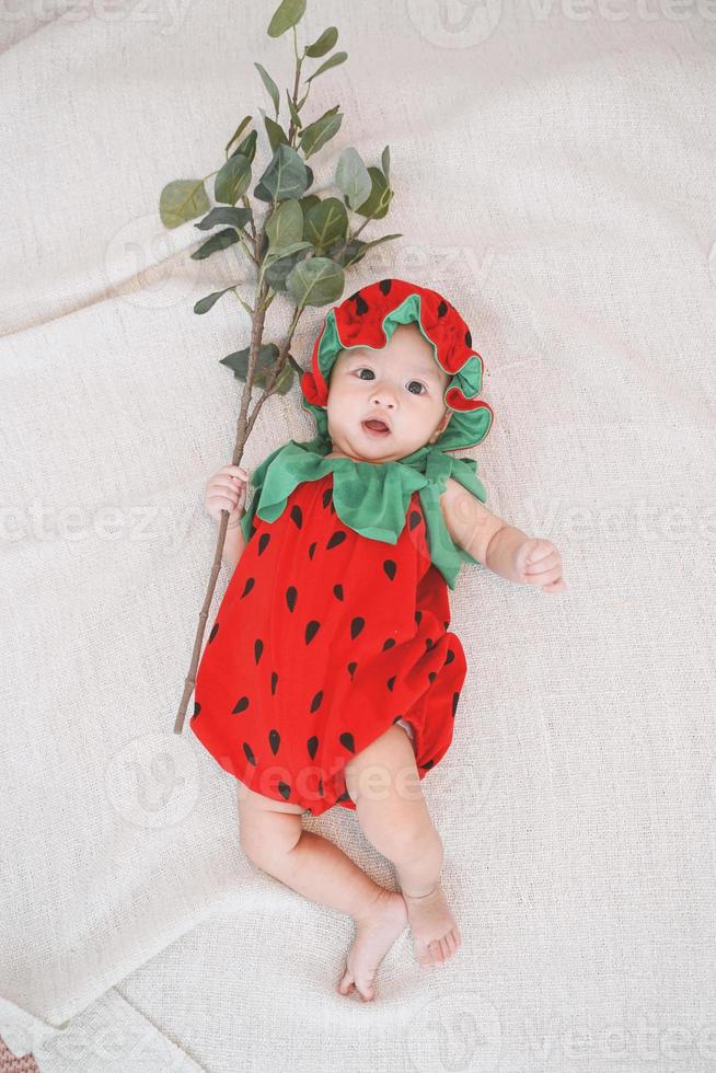 söt flicka klädd i en jordgubbe kostym och ligger på sängen och håller en gren. toppvy. foto