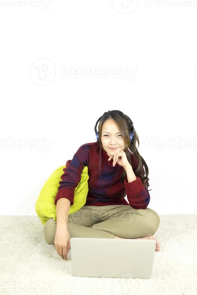 vacker stående ung asiatisk kvinna sitter på golvet med bärbar dator och hörlurar på vit bakgrund. foto