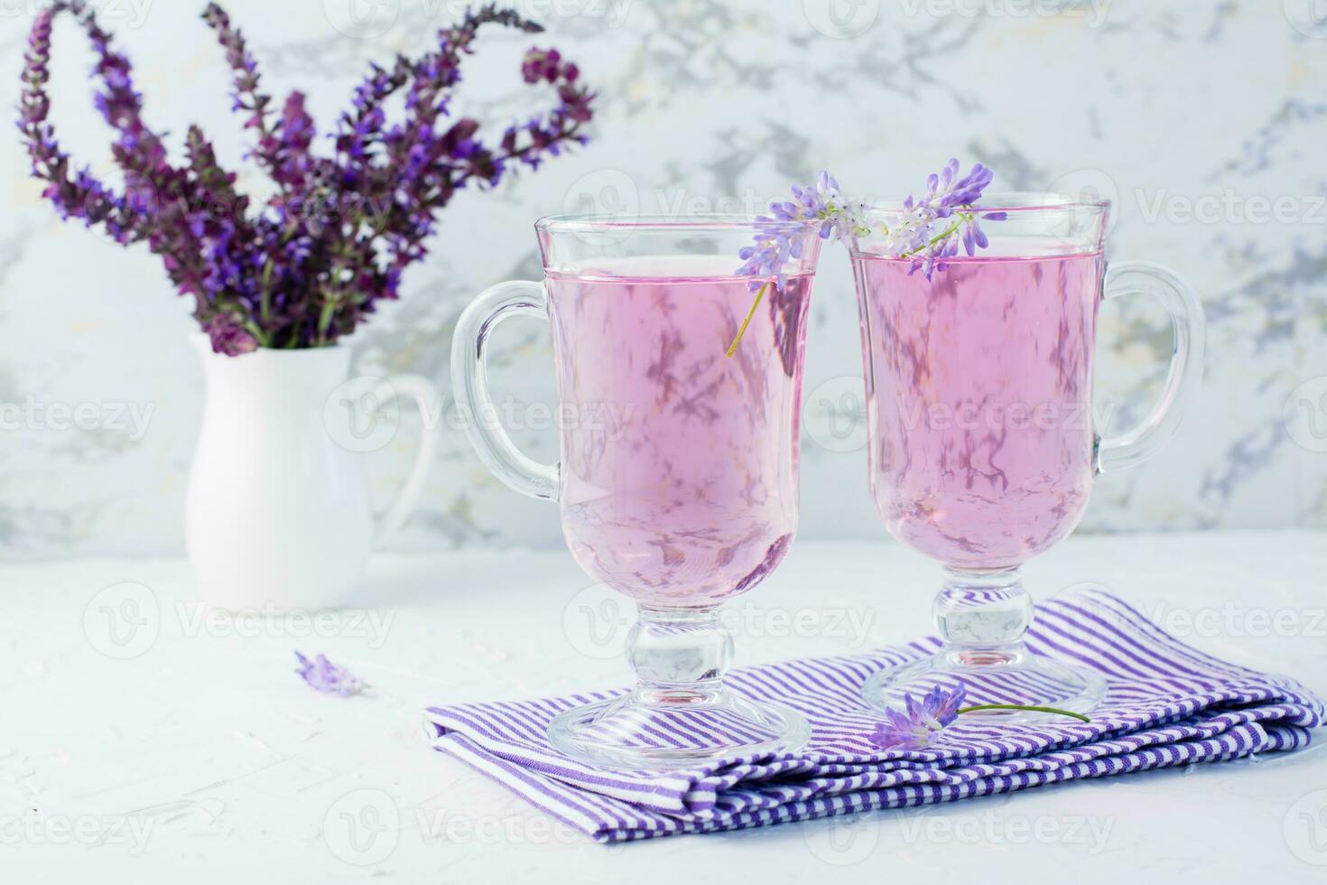 färsk vatten med lavendel- i glasögon och en bukett av blommor i en kanna på de tabell. lavendel- aromatisk cocktail foto