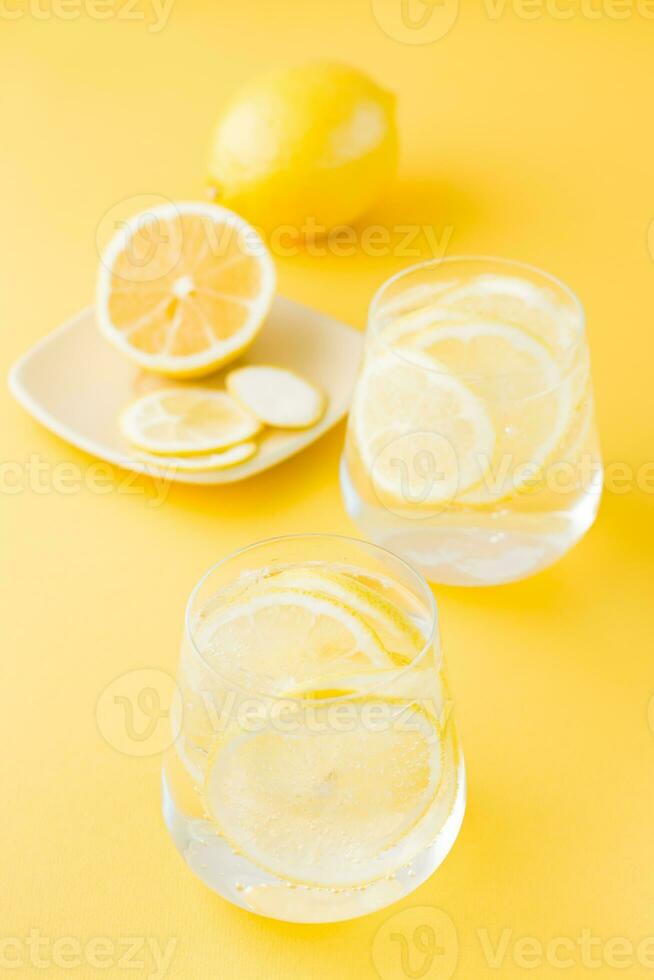 gnistrande vatten med citron- och is i glasögon och citron- skivor på en fat på en gul bakgrund. detox dryck. vertikal se foto