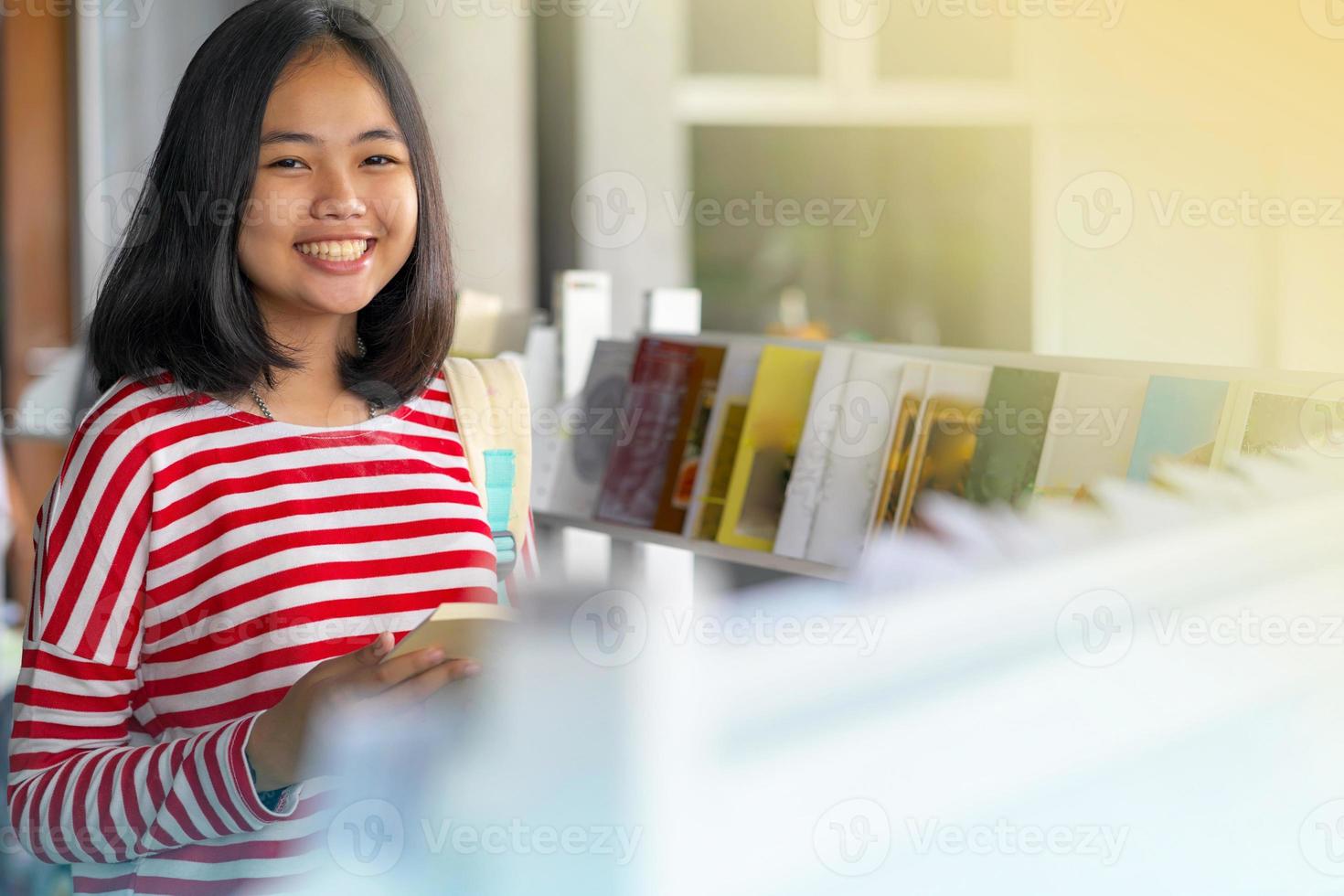 asiatisk tjej som står och ler och läser en bok i bokhandlarna foto