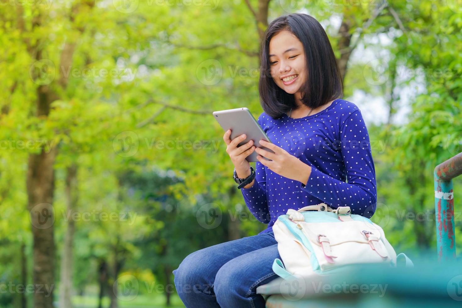 asiatisk studentflicka som använder en digital minnestavla i parkera en solig sommardag foto