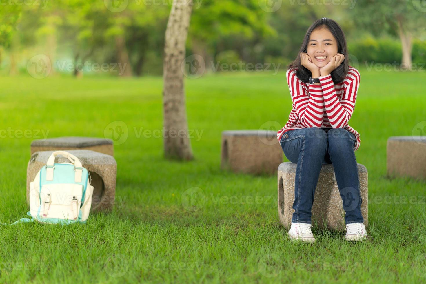 asiatisk studentflicka som sitter och ler i skolan parkerar en solig sommardag foto