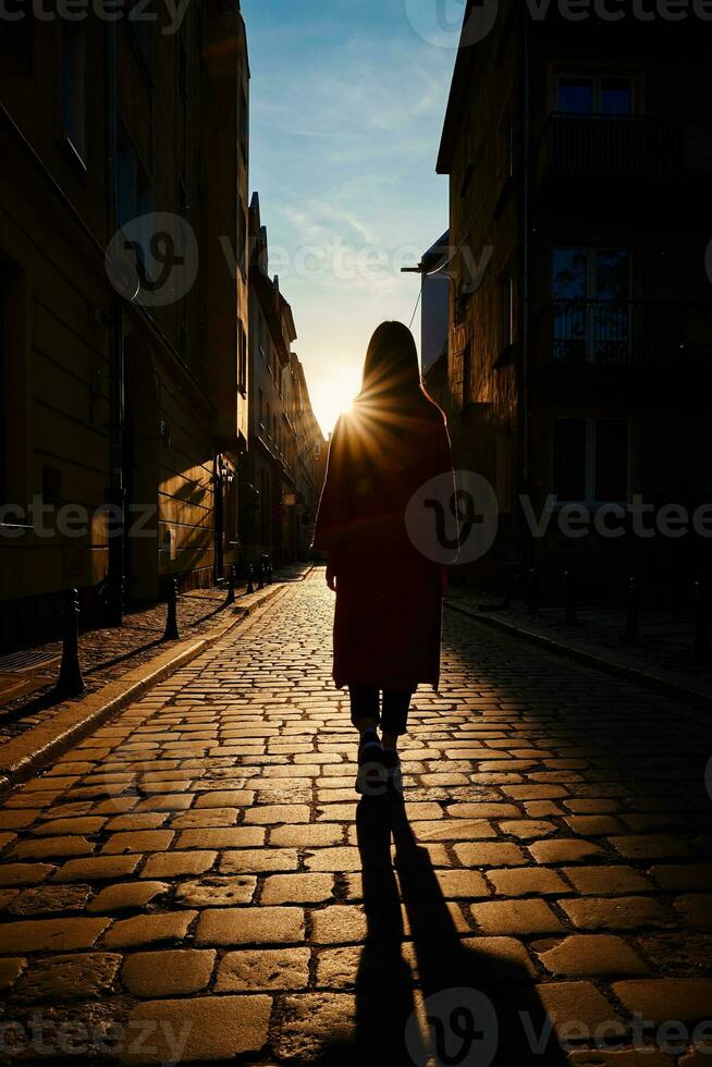 bak- se av kvinna gående på stad gata med solnedgång foto