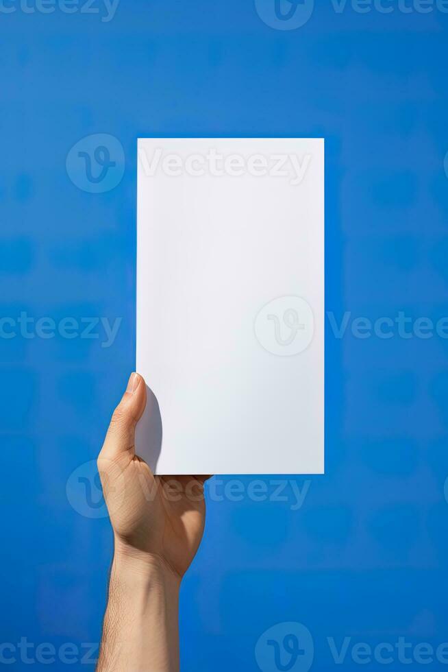 en mänsklig hand innehav en tom ark av vit papper eller kort isolerat på blå bakgrund. ai genererad foto