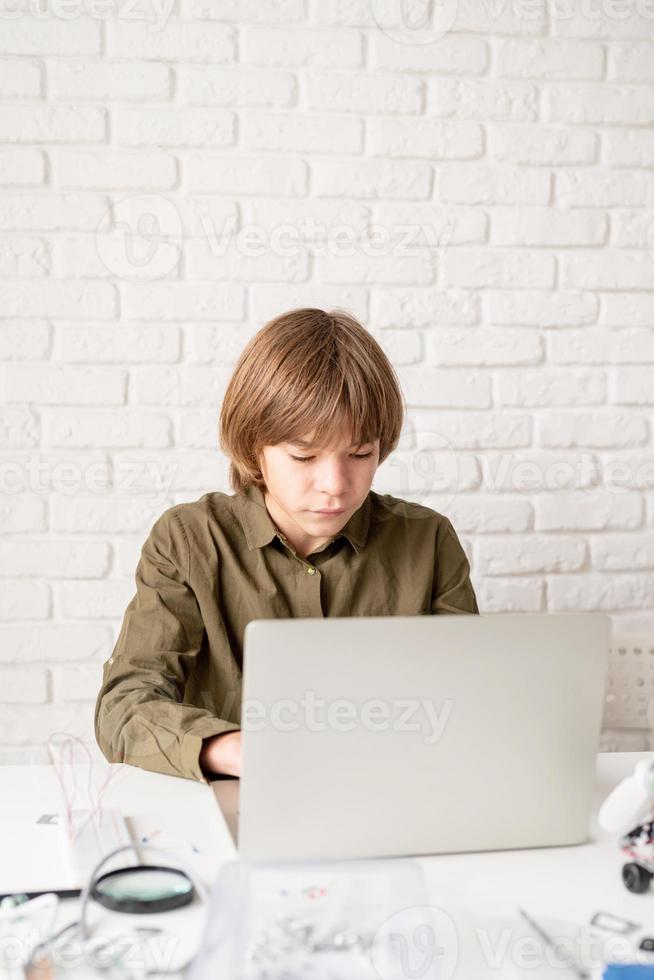 ung pojke som arbetar eller studerar på den bärbara datorn hemma foto