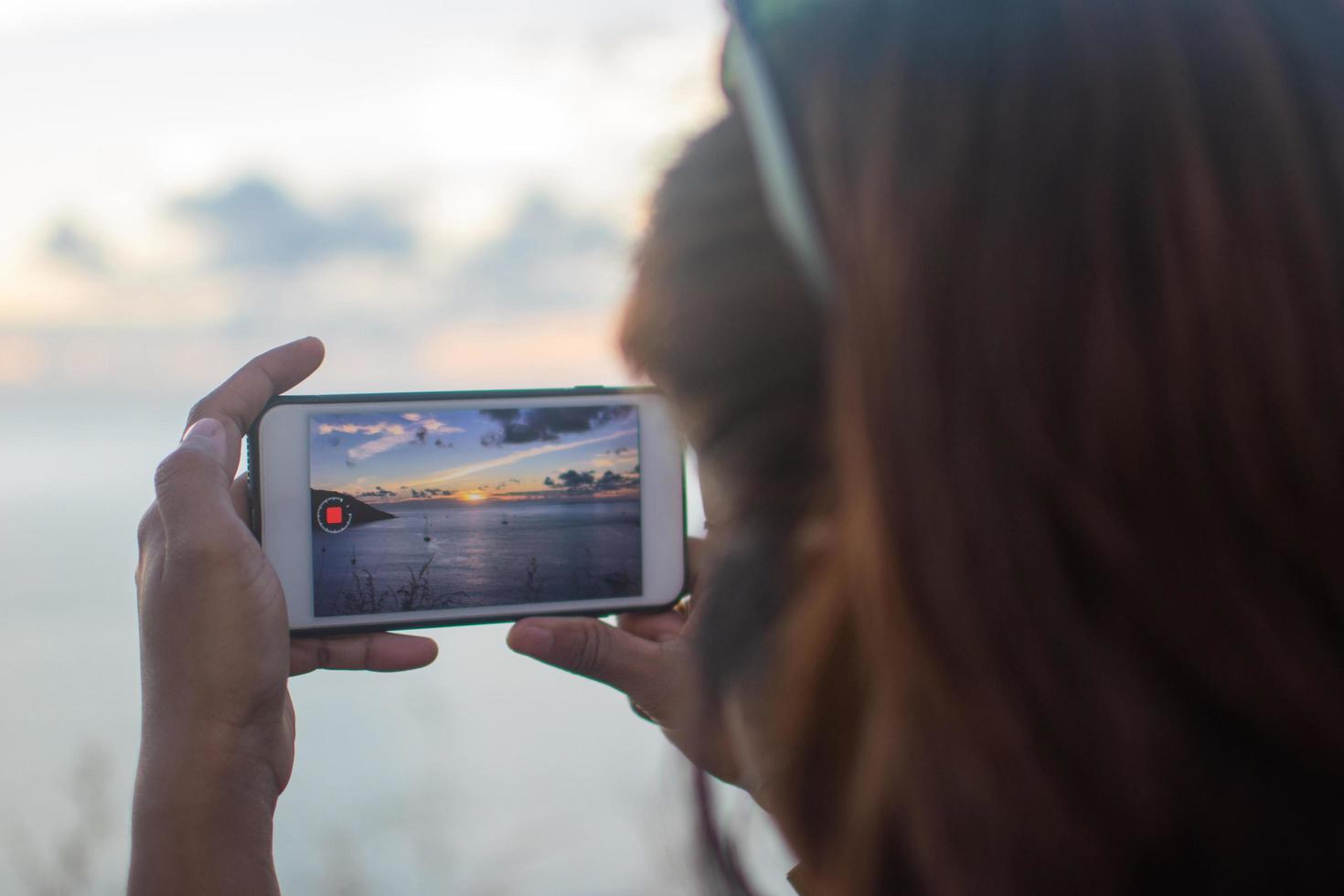 person som tar en video av solnedgången med smart telefon foto