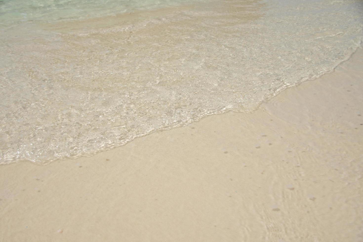 vacker mjuk våg på sand vid den soliga havet foto