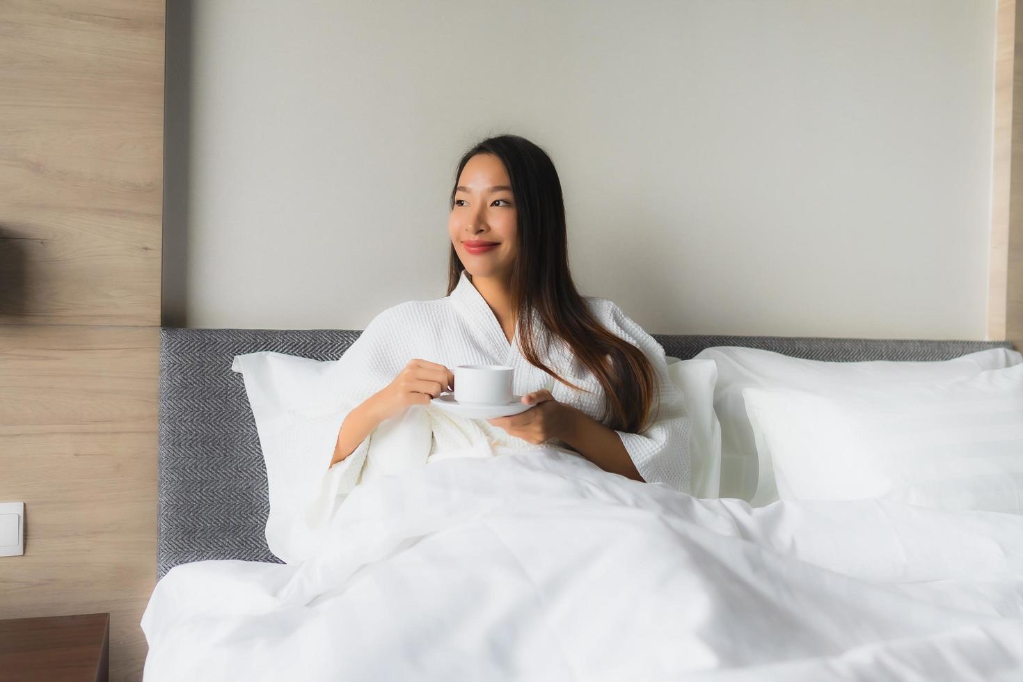 stående vackra unga asiatiska kvinnor med kaffekoppen på sängen foto
