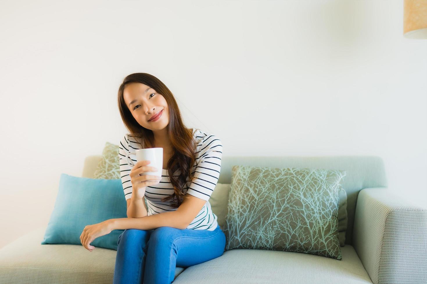 stående vacker ung asiatisk kvinna på soffan med kaffekoppen foto