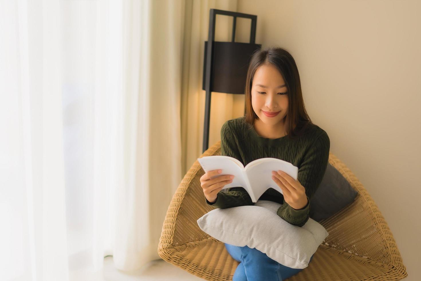 stående vackra unga asiatiska kvinnor som läser bok och sitter på soffstol foto