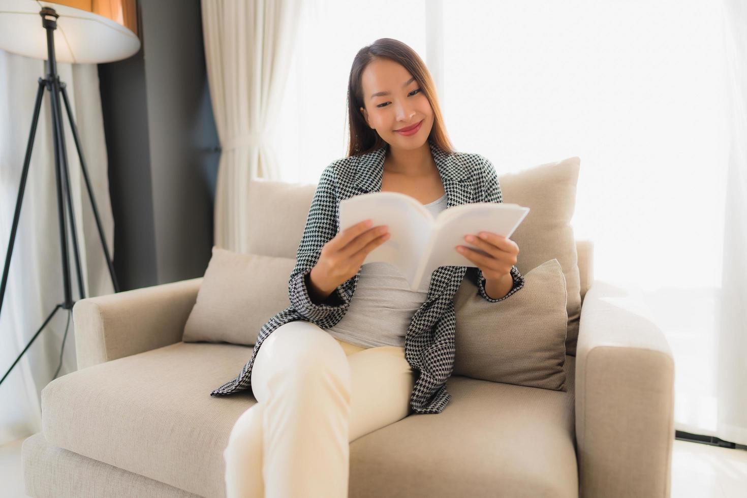 stående vackra unga asiatiska kvinnor som läser bok och sitter på soffstol foto