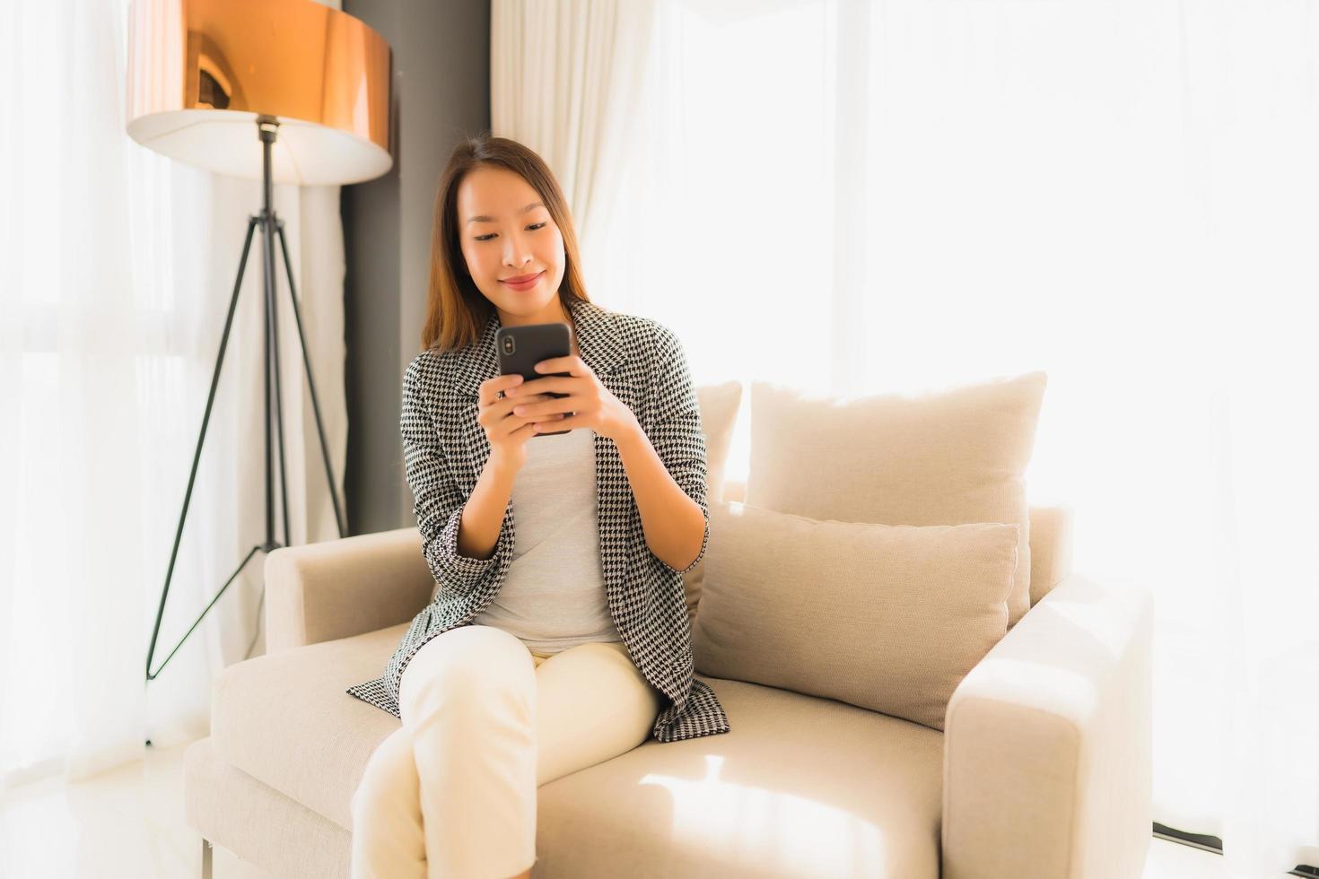 stående vackra unga asiatiska kvinnor som använder talande mobiltelefon och sitter på soffstol foto