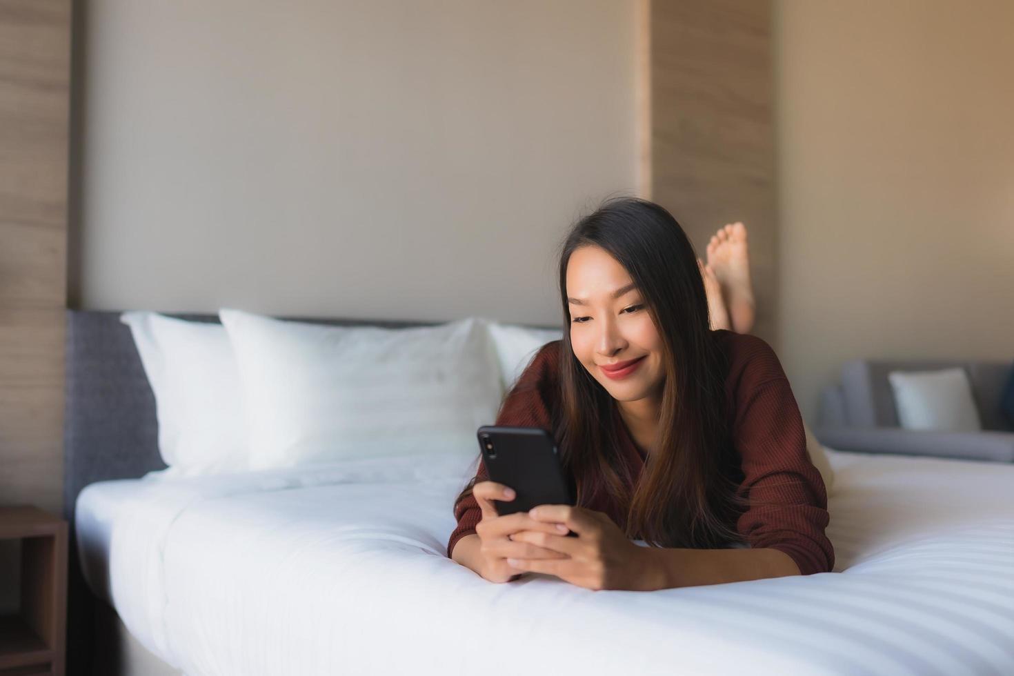 stående vackra unga asiatiska kvinnor som använder mobiltelefonen på sängen foto