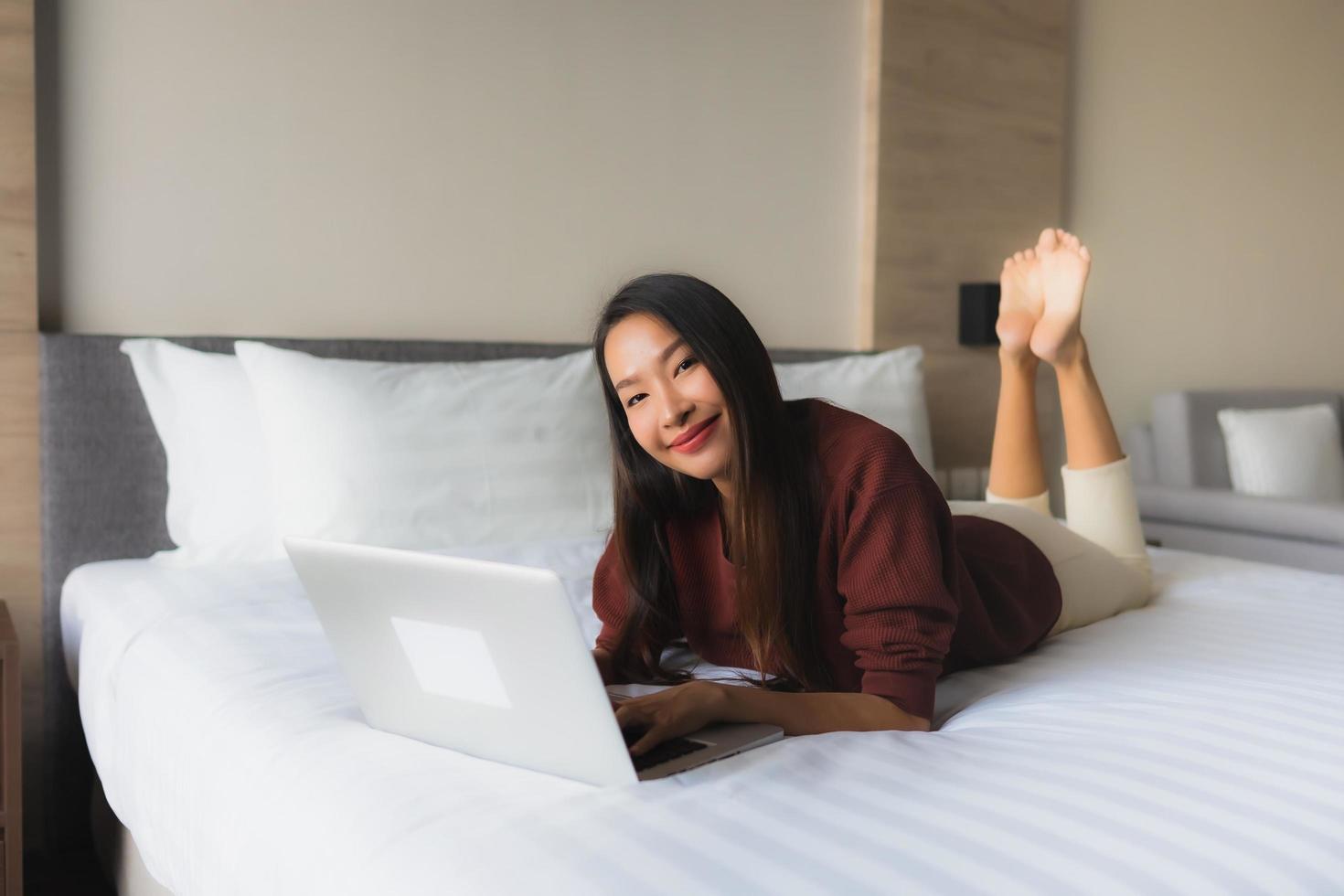 stående vackra unga asiatiska kvinnor som använder datorn och mobiltelefonen på sängen foto