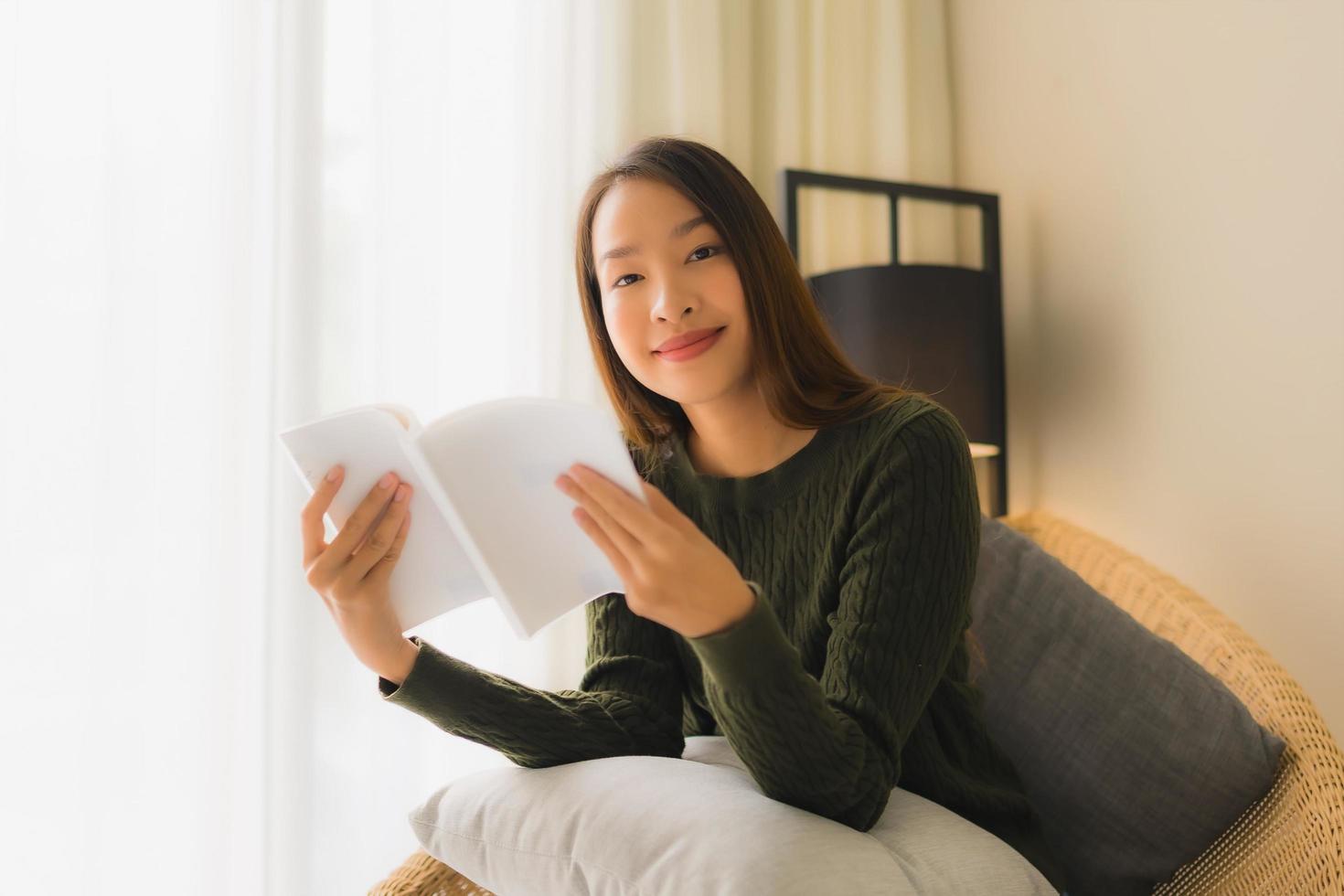 stående vackra unga asiatiska kvinnor som läser bok och sitter på soffstol foto