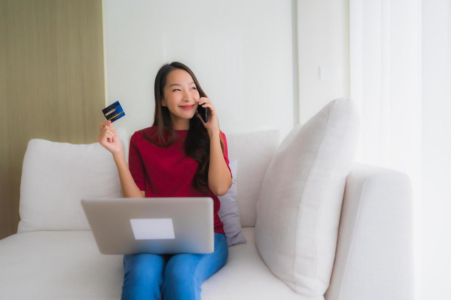 stående vackra unga asiatiska kvinnor som använder datorbärbar dator med mobiltelefon och kreditkort foto