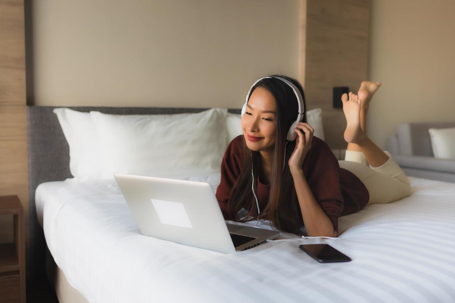 stående vackra unga asiatiska kvinnor som använder dator och hörlurar för att lyssna på musik foto