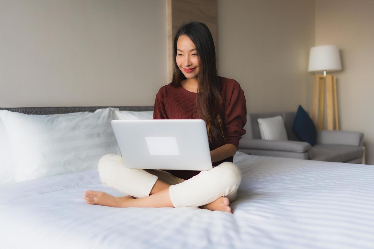 stående vackra unga asiatiska kvinnor som använder datorn och mobiltelefonen på sängen foto