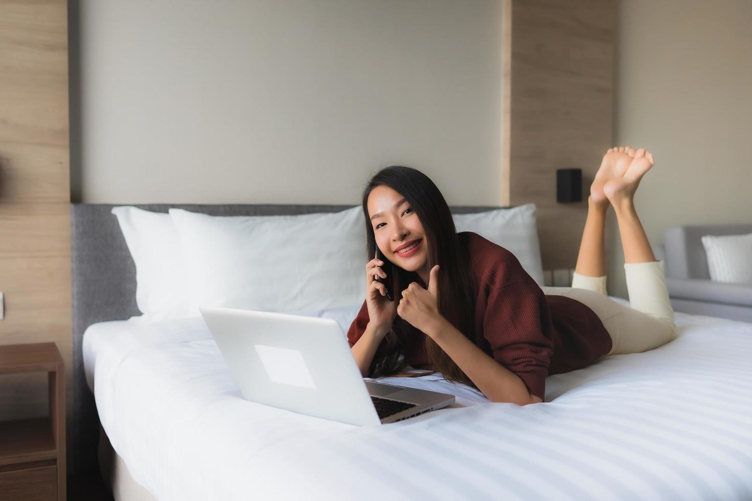 stående vackra unga asiatiska kvinnor som använder datorn och mobiltelefonen på sängen foto