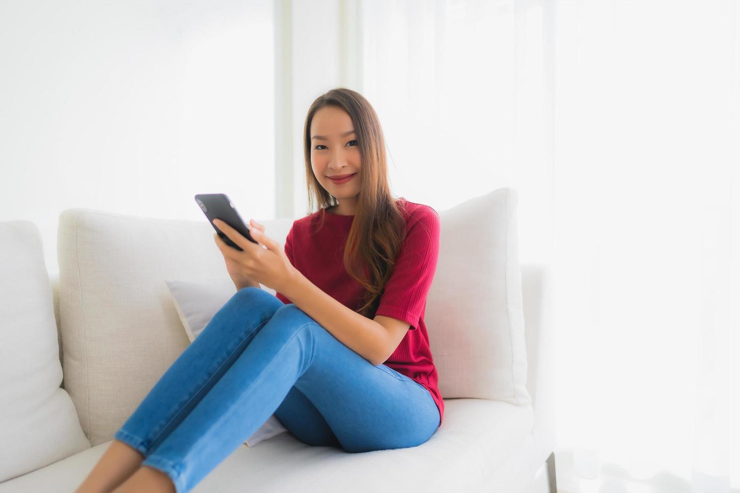 stående vackra unga asiatiska kvinnor som använder mobil eller smart telefon på soffan foto