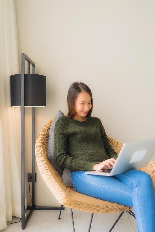 stående vackra unga asiatiska kvinnor som använder datorn eller bärbara datorn för att arbeta och sitta på soffstol foto