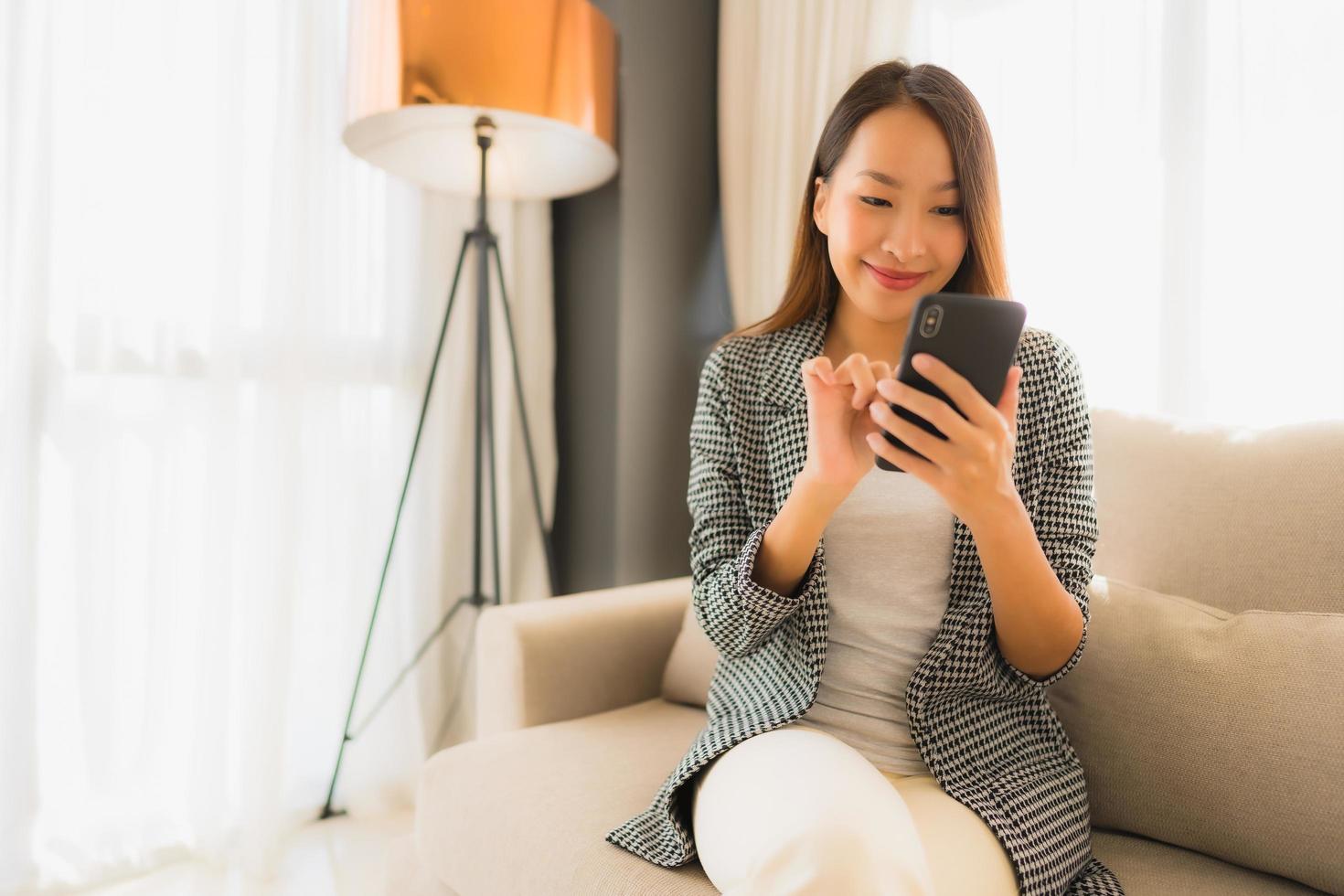 stående vackra unga asiatiska kvinnor som använder talande mobiltelefon och sitter på soffstol foto