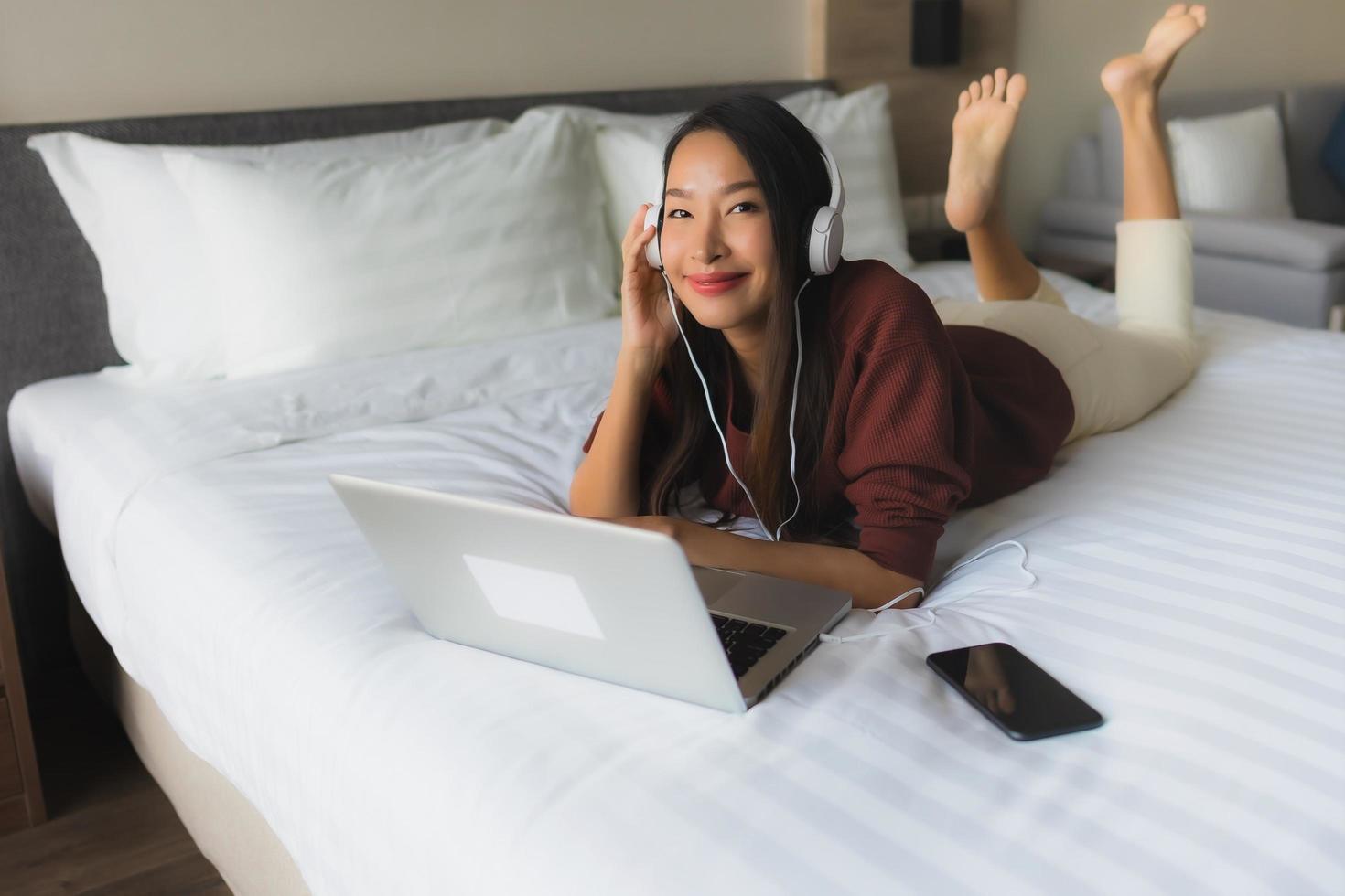 stående vackra unga asiatiska kvinnor som använder dator och hörlurar för att lyssna på musik foto