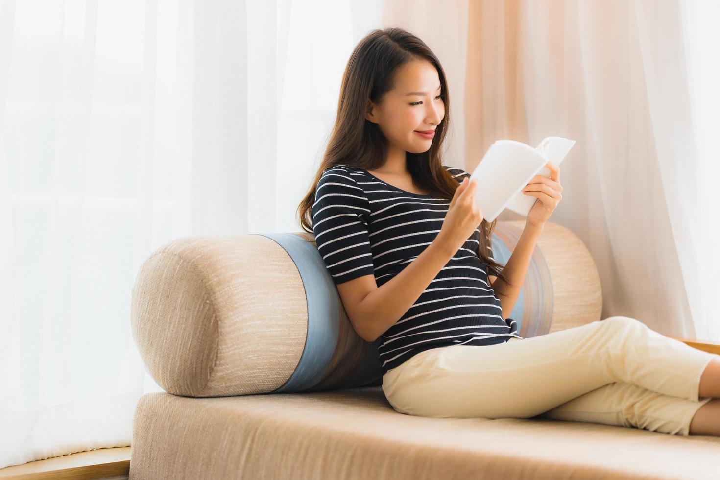 porträtt vacker ung asiatisk kvinna läser bok in på soffan i vardagsrummet foto