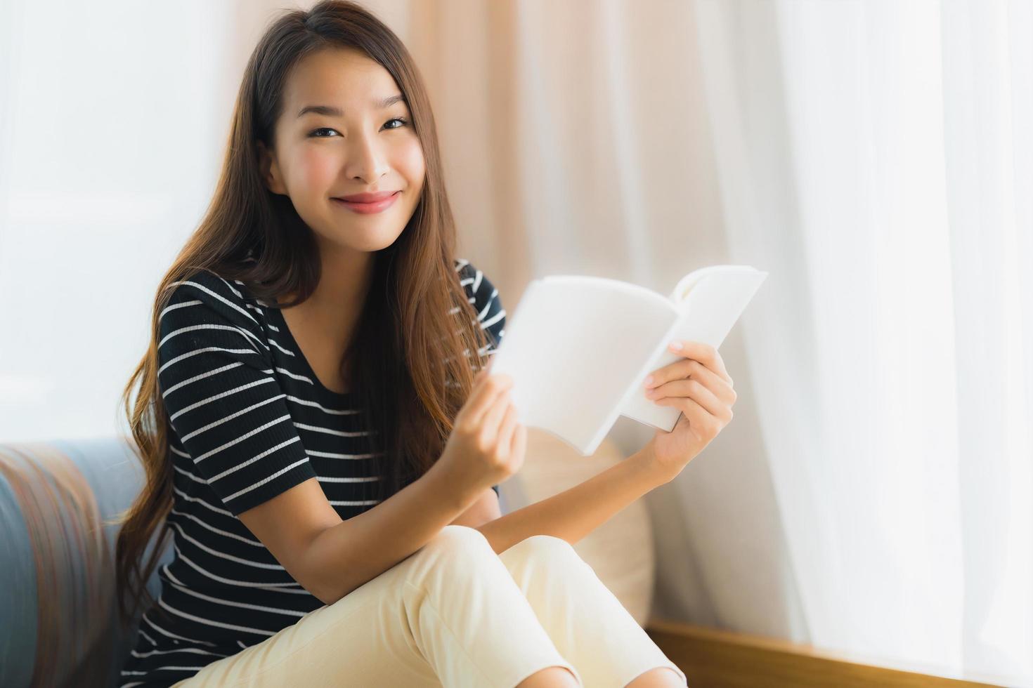 porträtt vacker ung asiatisk kvinna läser bok in på soffan i vardagsrummet foto