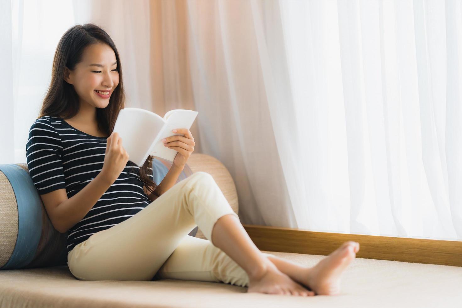 porträtt vacker ung asiatisk kvinna läser bok in på soffan i vardagsrummet foto