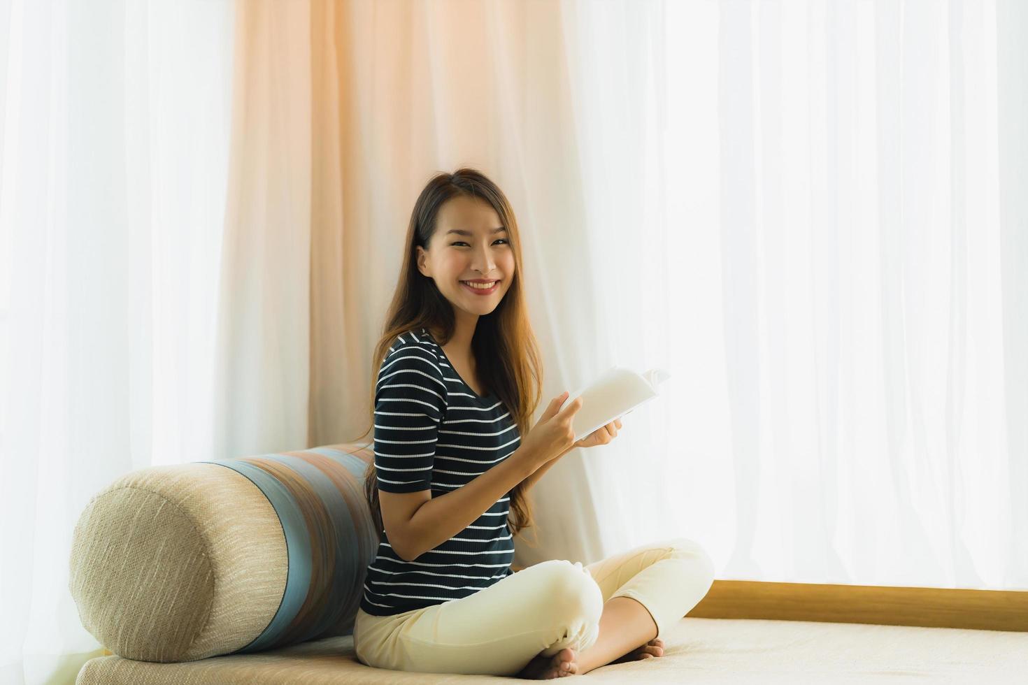 porträtt vacker ung asiatisk kvinna läser bok in på soffan i vardagsrummet foto