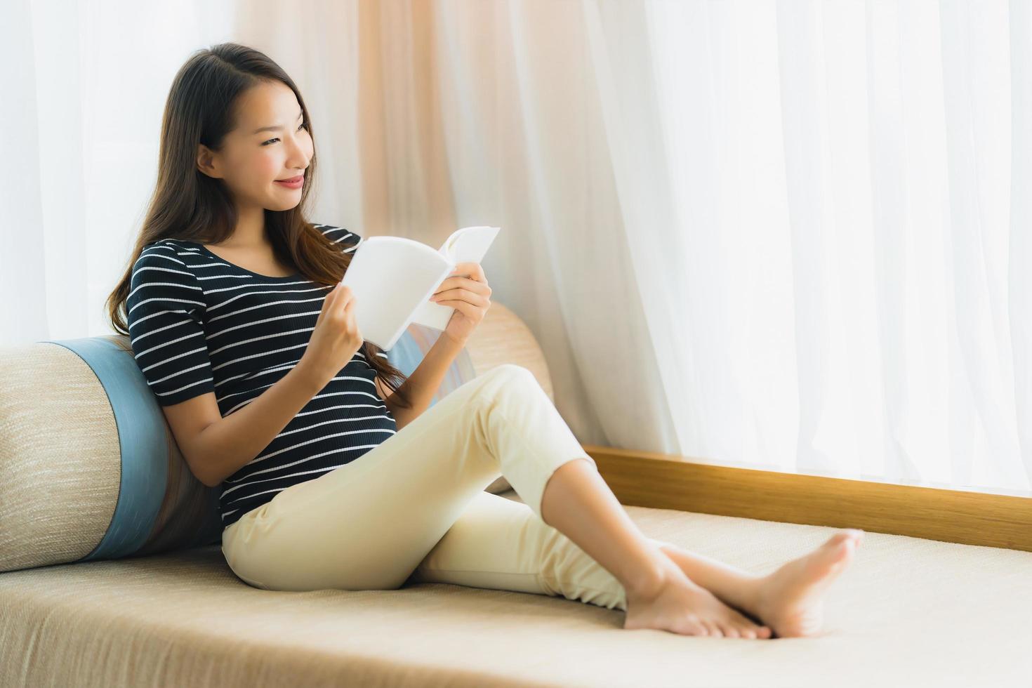 porträtt vacker ung asiatisk kvinna läser bok in på soffan i vardagsrummet foto