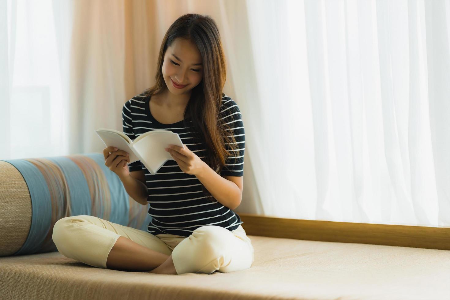 porträtt vacker ung asiatisk kvinna läser bok in på soffan i vardagsrummet foto