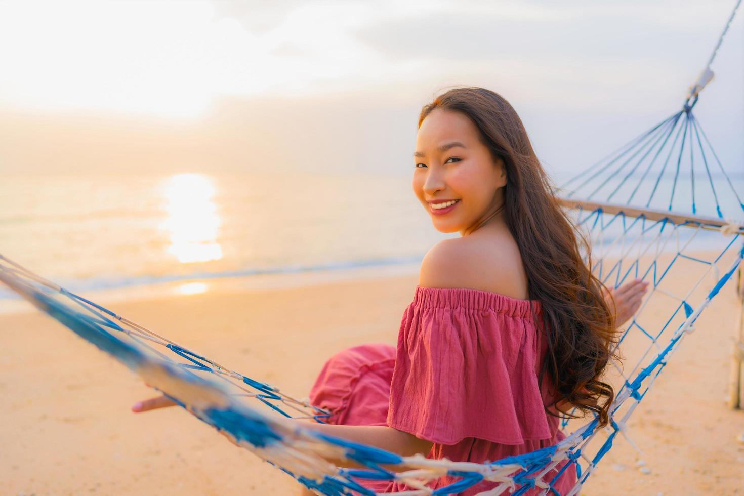 stående vacker ung asiatisk kvinna som sitter på hängmattan med leende glad neary strand hav och hav foto