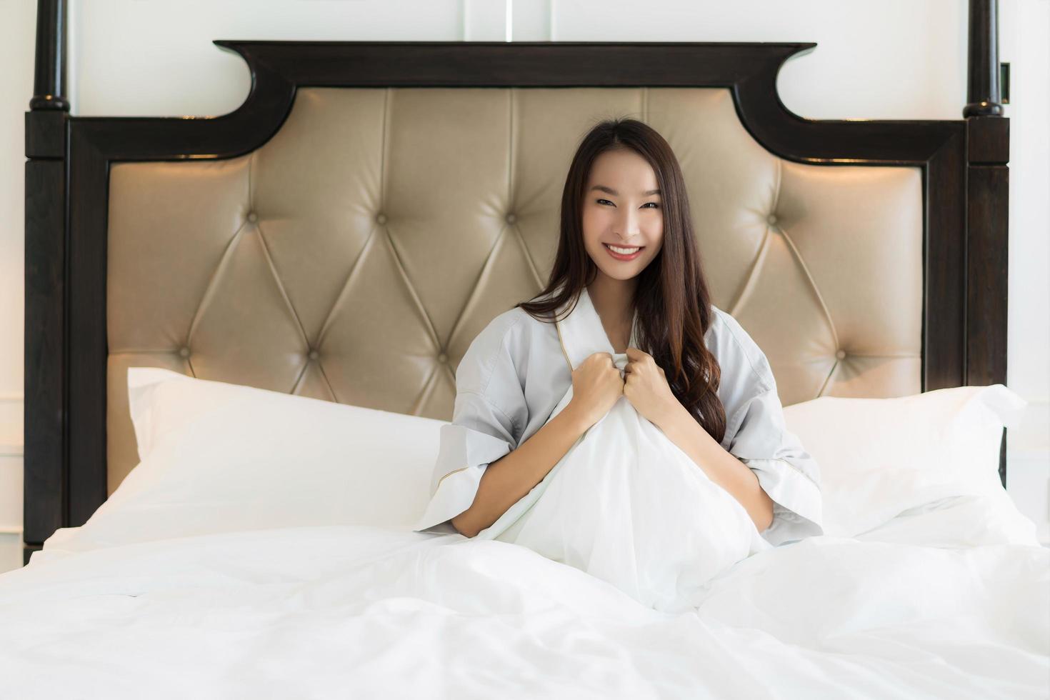 porträtt vacker ung asiatisk kvinna vaknar med glad och ler på sängen i sovrum interiör foto