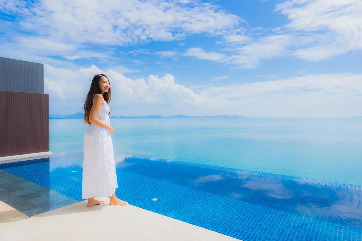 stående ung asiatisk kvinna koppla av leende glad runt poolen i hotellet och resort foto