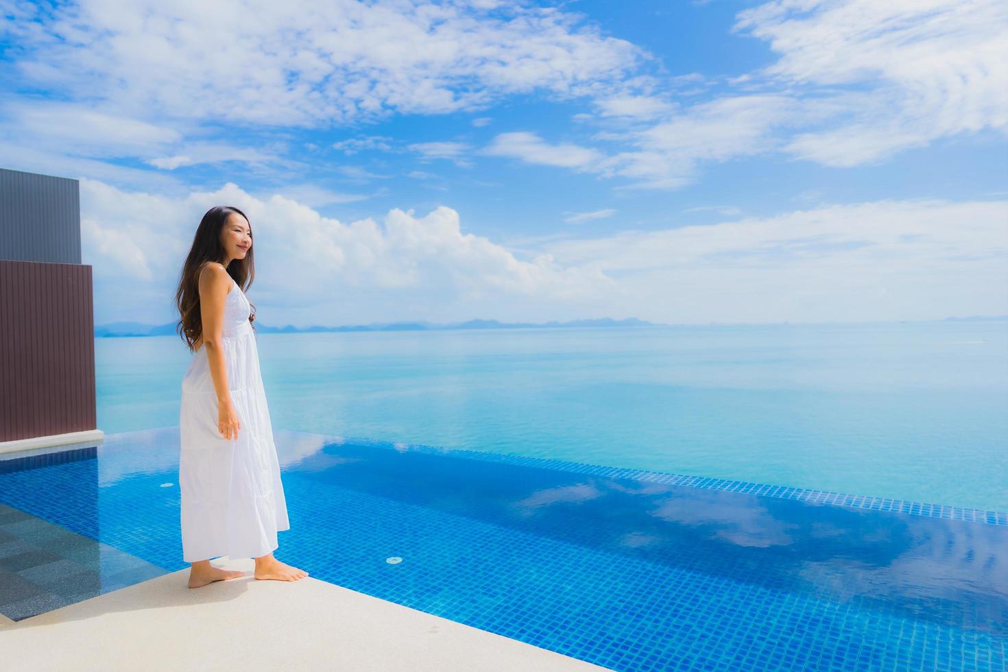 stående ung asiatisk kvinna koppla av leende glad runt poolen i hotellet och resort foto