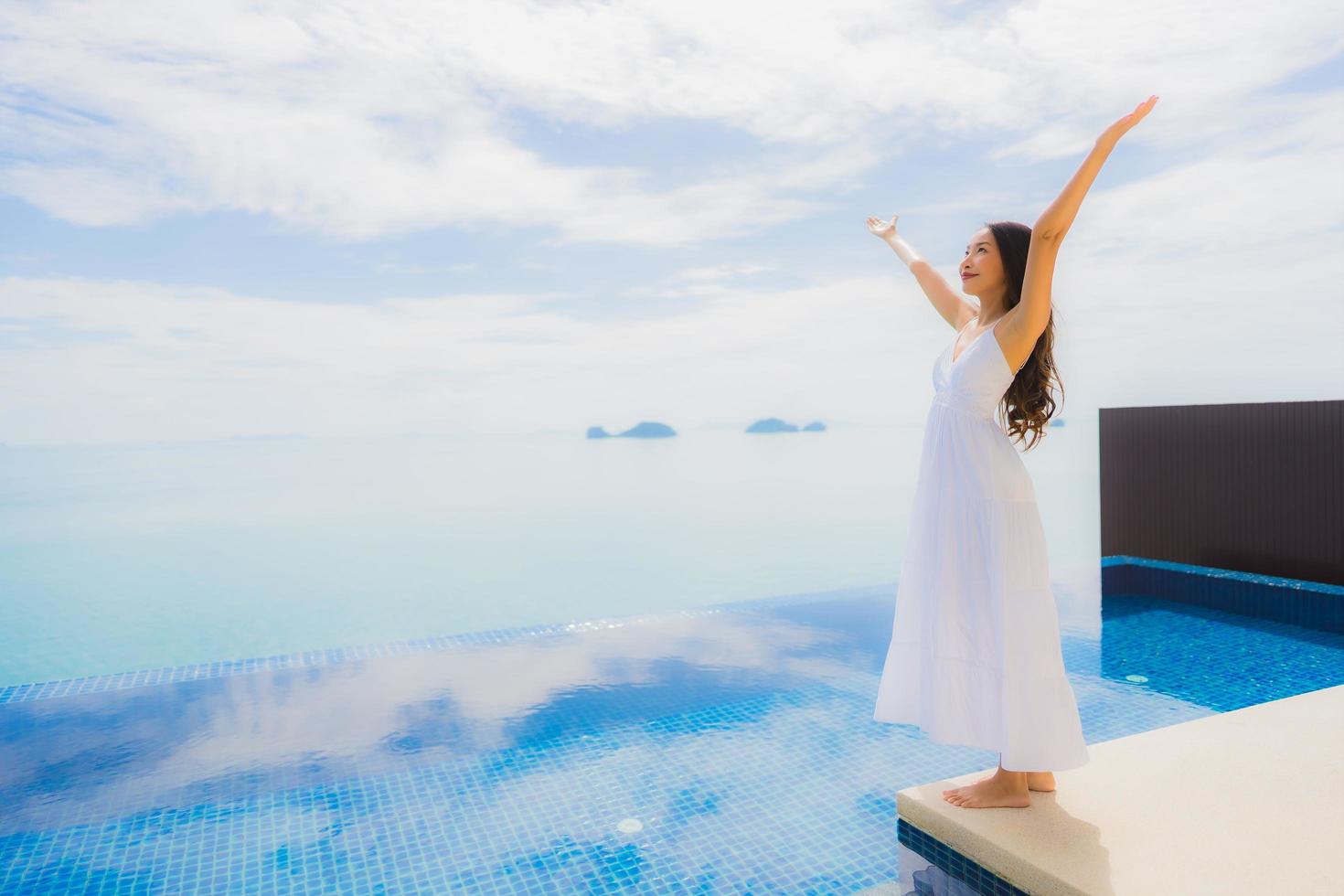 stående ung asiatisk kvinna koppla av leende glad runt poolen i hotellet och resort foto