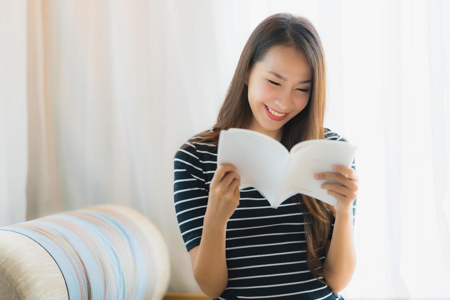 porträtt vacker ung asiatisk kvinna läser bok in på soffan i vardagsrummet foto