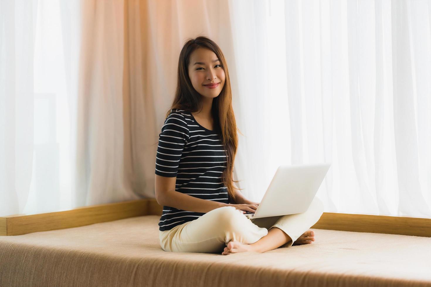 stående härlig ung asiatisk kvinna som använder datoranteckningsboken eller bärbar dator på soffan i vardagsrummet foto