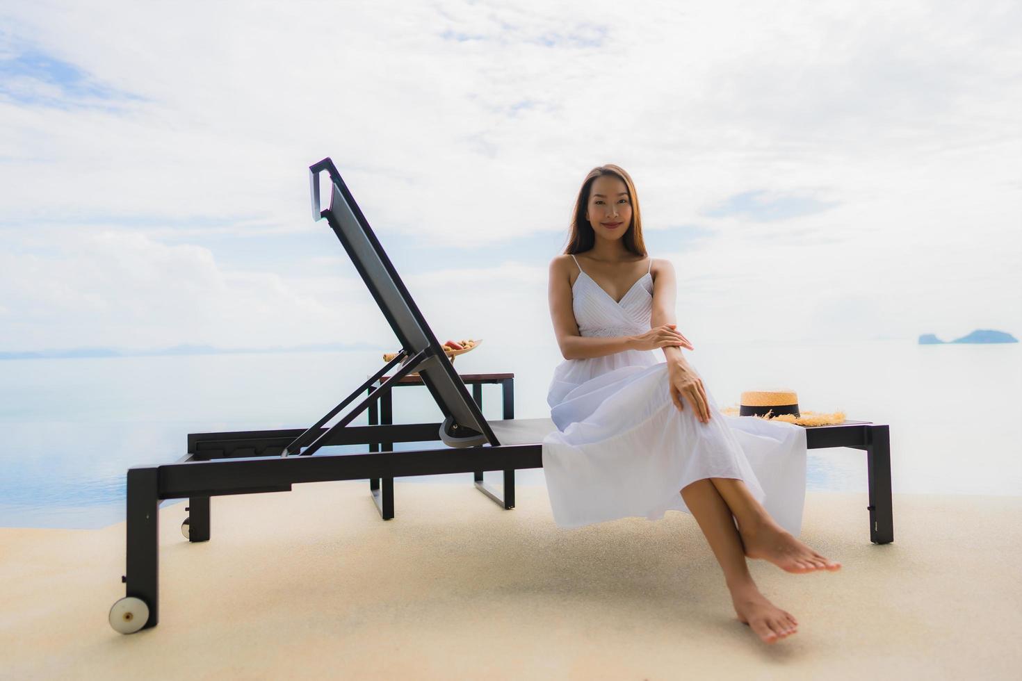 stående ung asiatisk kvinna koppla av leende glad runt poolen i hotellet och resort foto