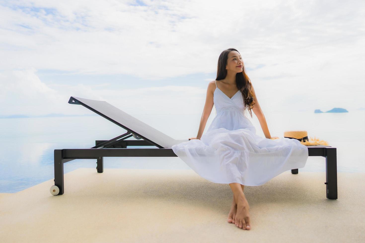 stående ung asiatisk kvinna koppla av leende glad runt poolen i hotellet och resort foto